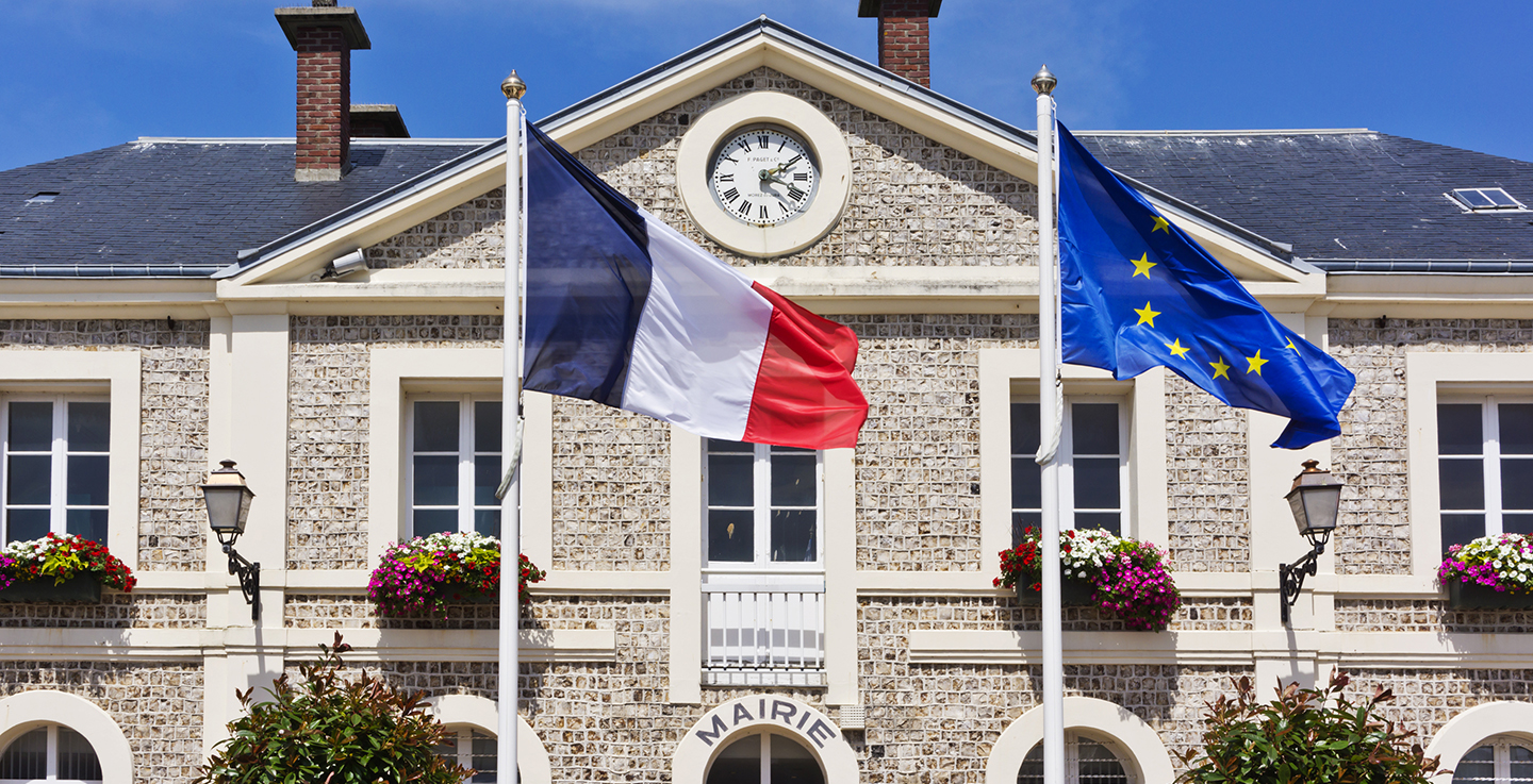 Façade d'une mairie et de son horloge avec ses drapeaux français et européens